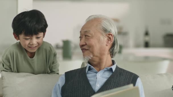 Азиатский Дедушка Внук Разговаривают Читая Книгу — стоковое видео