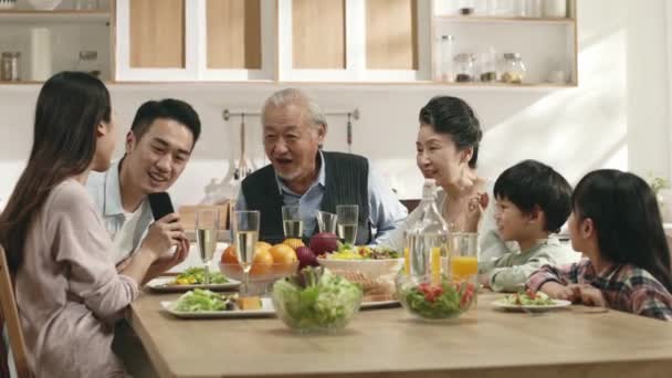一緒に食事をしながら家族に携帯電話で写真を見せる若いアジア人女性 — ストック動画