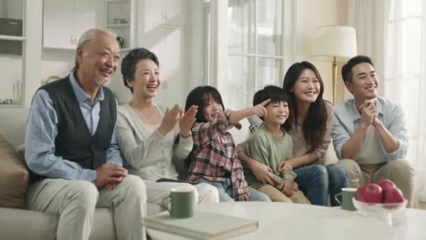 三代亚洲家庭坐在客厅的沙发上看电视 — 图库视频影像