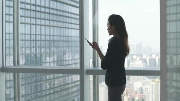 Młody Azji Bizneswoman Patrząc Telefon Komórkowy Przez Okno Nowoczesny Biuro — Wideo stockowe