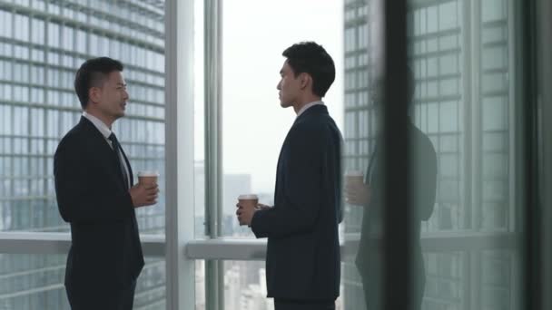 Dwóch Azjatyckich Biznesmenów Stojących Przy Oknie Rozmawiających Rozmawiających Nowoczesnym Biurze — Wideo stockowe