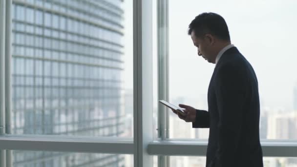 Asiatischer Geschäftsmann Schaut Auf Handy Während Büro Fenster Vorbeigeht — Stockvideo