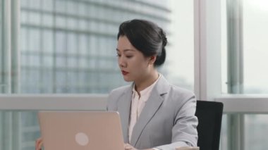 Genç Asyalı iş kadını ofiste dizüstü bilgisayar ve cep telefonu kullanarak çalışıyor.