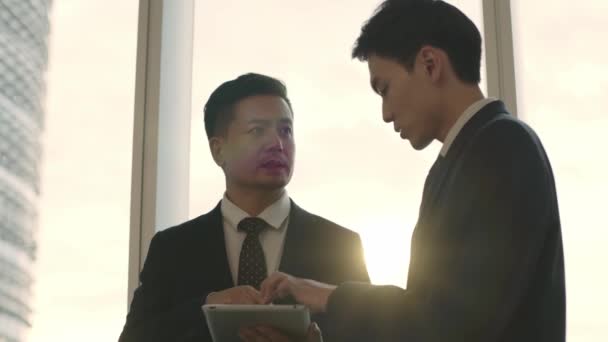 Two Asian Businessmen Standing Window Office Discussing Business Using Digital — Stock Video