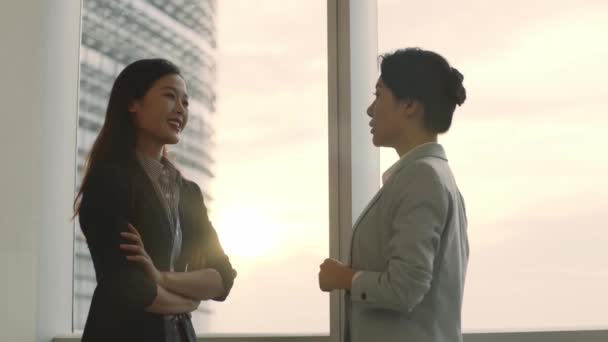 オフィスの窓のそばに立っておしゃべりをしているアジア系の2人が — ストック動画
