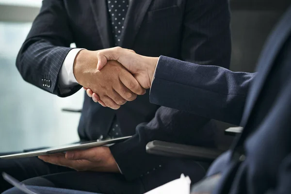 2人のアジア人ビジネスマンが椅子に座りオフィスで握手をし — ストック写真