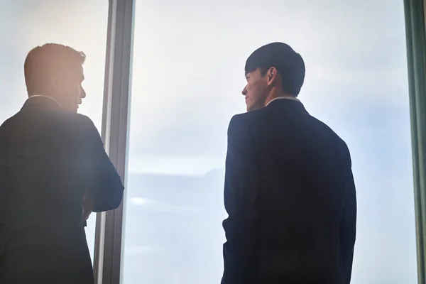 Два Азиатских Бизнесмена Коллеги Стоят Окна Разговаривая Обсуждая Взгляде Город — стоковое фото