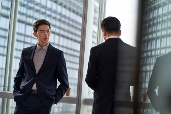 Два Азиатских Бизнесмена Коллеги Стоят Окна Разговаривая Обсуждая Взгляде Город — стоковое фото