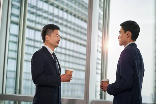 Dva Asijští Podnikatelé Stojící Okna Moderní Kanceláři Kteří Vedou Rozhovor — Stock fotografie