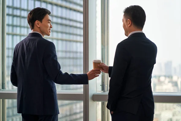 在现代办公室的橱窗前 年轻的亚洲商人把一杯咖啡递给同事的后视镜 — 图库照片