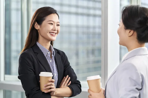 現代のオフィスで窓のそばでおしゃべりをしている若いアジア系ビジネス女性2人 — ストック写真