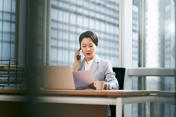在现代办公室工作的年轻亚洲女商人 使用笔记本电脑和手机 — 图库照片