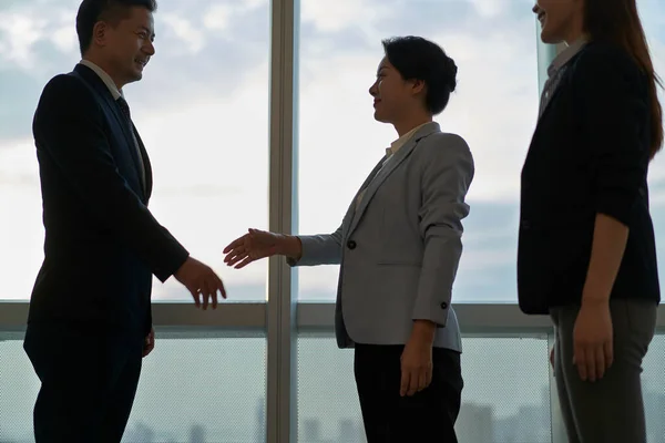 オフィスの窓から客と握手するアジア人のビジネスマン — ストック写真