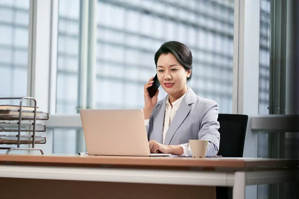 在现代办公室工作的年轻亚洲女商人 使用笔记本电脑和手机 — 图库照片