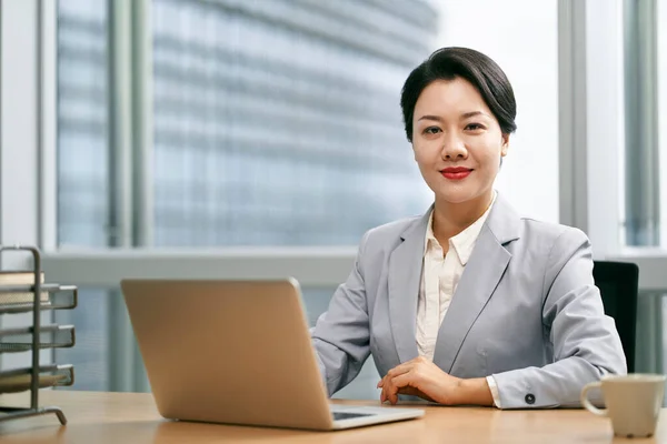 ラップトップコンピュータを使って現代のオフィスで働く成功した若いアジアのビジネス女性 — ストック写真