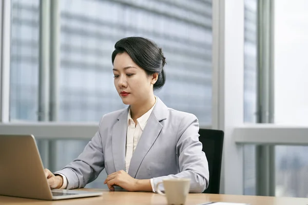 使用手提电脑在现代办公室工作的年轻亚洲女商人 — 图库照片