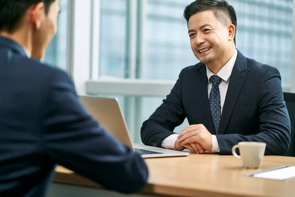 Два Азиатских Бизнесмена Сидящих Столом Лицом Лицу Современном Офисе Обсуждающих — стоковое фото