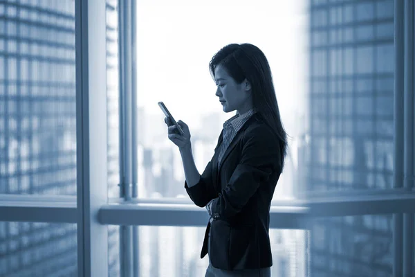Młody Azji Biznes Kobieta Stojąc Przy Okno Patrząc Telefon Komórkowy — Zdjęcie stockowe