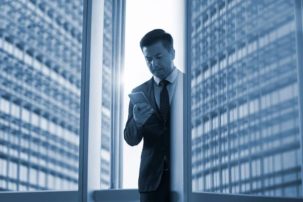 Азіатський Бізнесмен Дивиться Мобільний Телефон Офісі Сучасною Будівлею Задньому Плані — стокове фото
