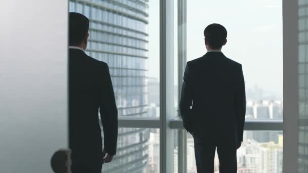 オフィスの窓の外の街を見ながら話している2人のアジア人ビジネスマン — ストック動画