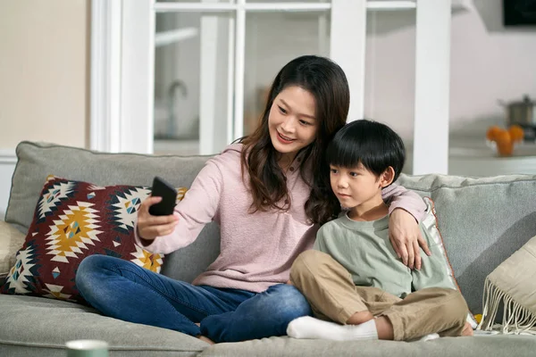 快乐的亚洲母亲和儿子坐在家里的沙发上 用手机自拍 — 图库照片