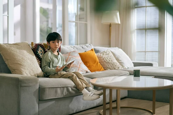 亚洲小男孩坐在家里客厅的沙发上 看着摄像机 — 图库照片