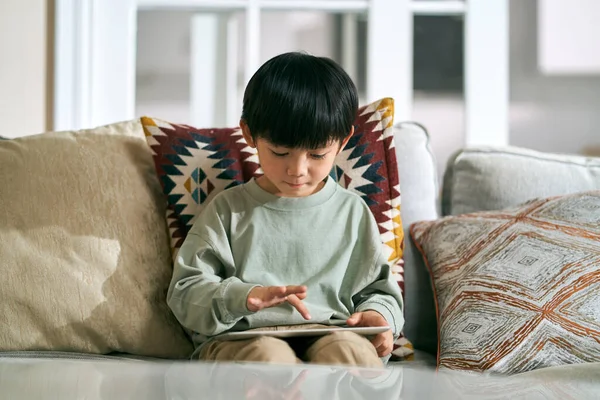 5歳の小さなアジアの少年がデジタルタブレットコンピュータを使って自宅のソファに座って — ストック写真