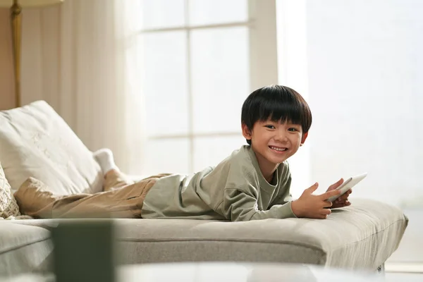 かわいいアジアの男の子横たわっ上の家族ソファにホームを保持デジタルタブレット — ストック写真