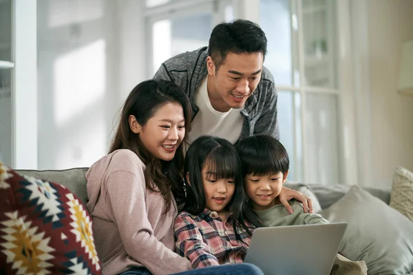 幸せな若いアジアのカップル2人の子供と一緒にラップトップコンピュータを使用して自宅で家族のソファに座っている — ストック写真