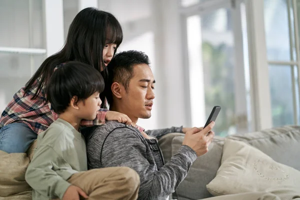 Młody Azjatycki Ojciec Dwoje Dzieci Siedzi Kanapie Rodzinnej Domu Patrząc — Zdjęcie stockowe