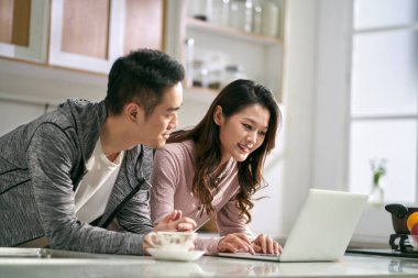 Genç Asyalı çift evdeki aile mutfağında dizüstü bilgisayar kullanıyor.