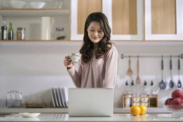 家庭でノートパソコンを使って台所で働く若いアジア系女性のフリーランス — ストック写真