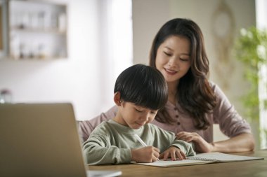 Genç Asyalı anne evde oturup oğluna çalışmasında yardım ediyor.