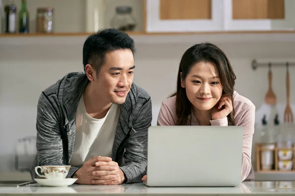 家庭の家庭用キッチンでノートパソコンを使っている若いアジア人のカップルは — ストック写真