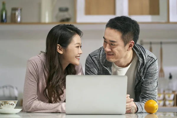 家庭の家庭用キッチンでノートパソコンを使っている若いアジア人のカップルは — ストック写真