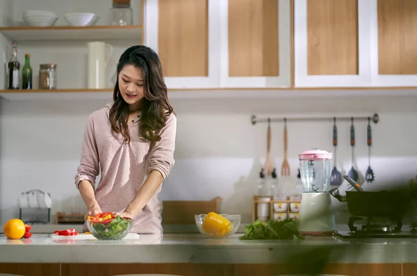 若いアジア系女性の主婦が自宅のキッチンでサラダを作る — ストック写真
