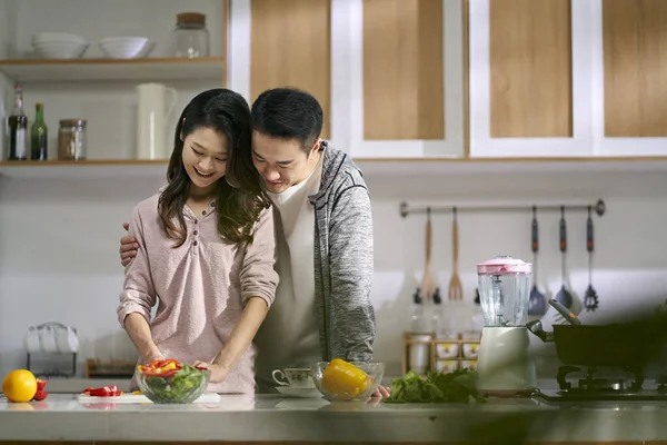 快乐的爱着一对年轻的亚洲夫妇在家里的厨房里一起做饭 — 图库照片