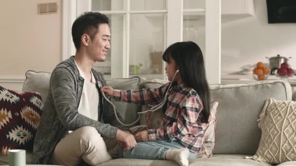 若いアジア人の父と小学生の娘は家で医者と患者と遊ぶのが楽しい — ストック動画