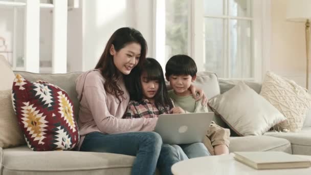 아시아인 어머니와 자녀가 가족용 소파에 노트북 컴퓨터를 있습니다 — 비디오