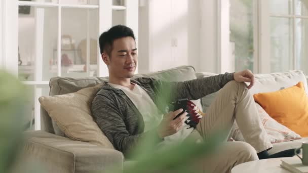 Joven Asiático Hombre Sentado Sofá Casa Mirando Teléfono Celular — Vídeo de stock