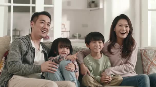 有两个孩子坐在家里沙发上看电视的快乐的亚洲家庭 — 图库视频影像
