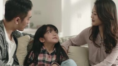 Genç Asyalı ebeveynler evdeki aile koltuğunda oturup kızlarıyla hoş sohbetler ediyorlar.