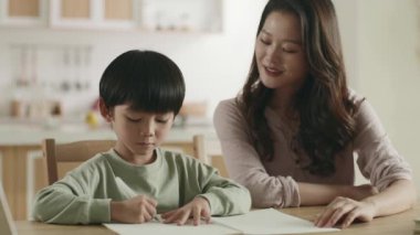Genç Asyalı anne oğluna ev ödevinde yardım ediyor.