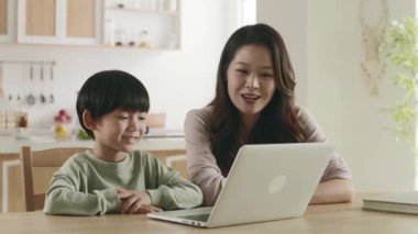 Genç Asyalı anne, oğluyla birlikte dizüstü bilgisayar kullanarak film izliyor.