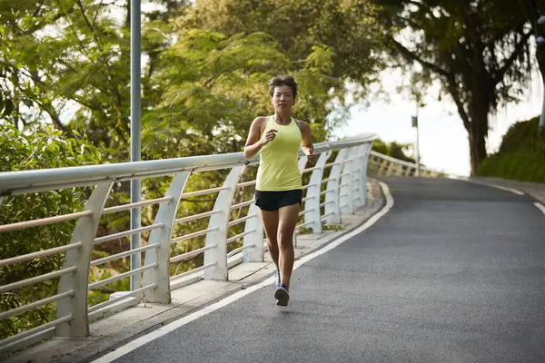 年轻的亚洲女人女慢跑者在城市公园的室外锻炼 图库照片