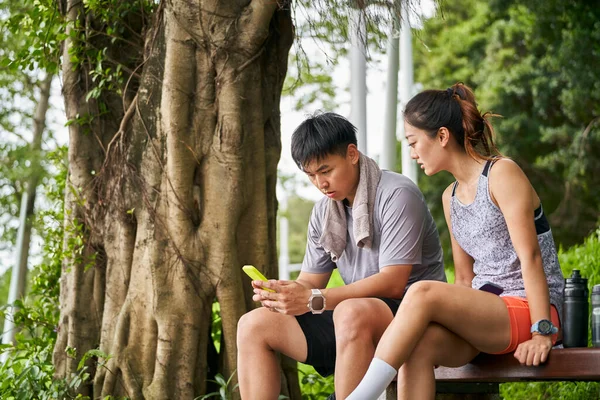 年轻的亚洲夫妇在户外运动中休息时分享手机照片 免版税图库图片