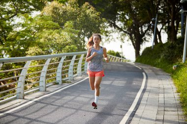 Genç Asyalı kadın parkta koşuyor.