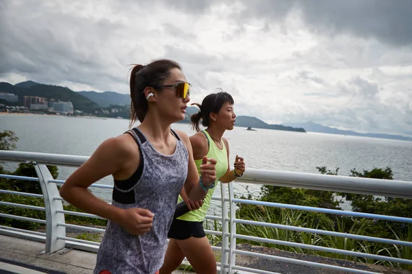两名年轻的亚洲女子慢跑者在海边的公园里跑步 图库照片