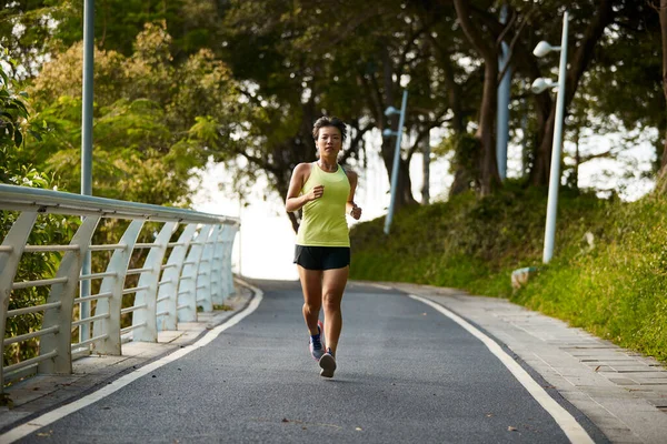 年轻的亚洲女人女慢跑者在城市公园的室外锻炼 图库图片