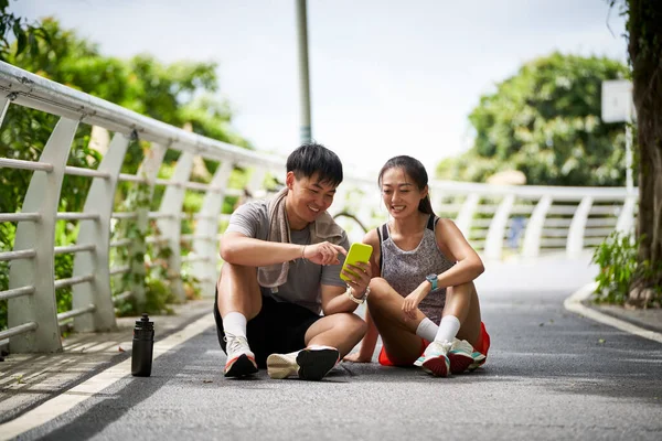 年轻的亚洲夫妇在户外运动时一边看手机照片一边休息 图库图片